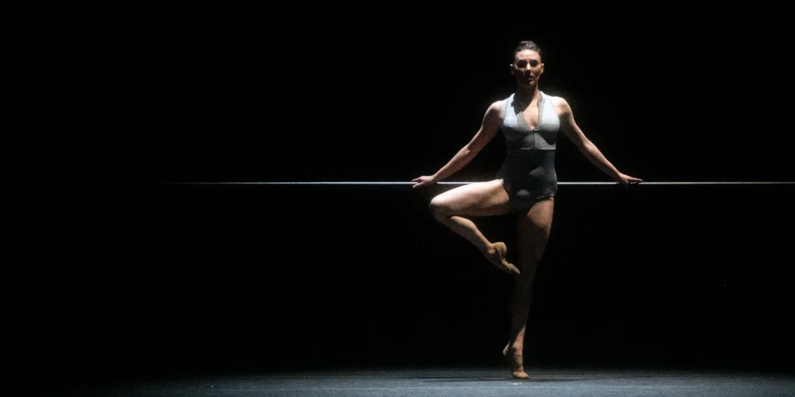 Turn It Out With Tiler Peck & Friends Review featuring the prima ballerina in a grey leotard, legs bare, with a ballet barre in the background.