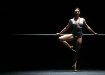 Turn It Out With Tiler Peck & Friends Review featuring the prima ballerina in a grey leotard, legs bare, with a ballet barre in the background.