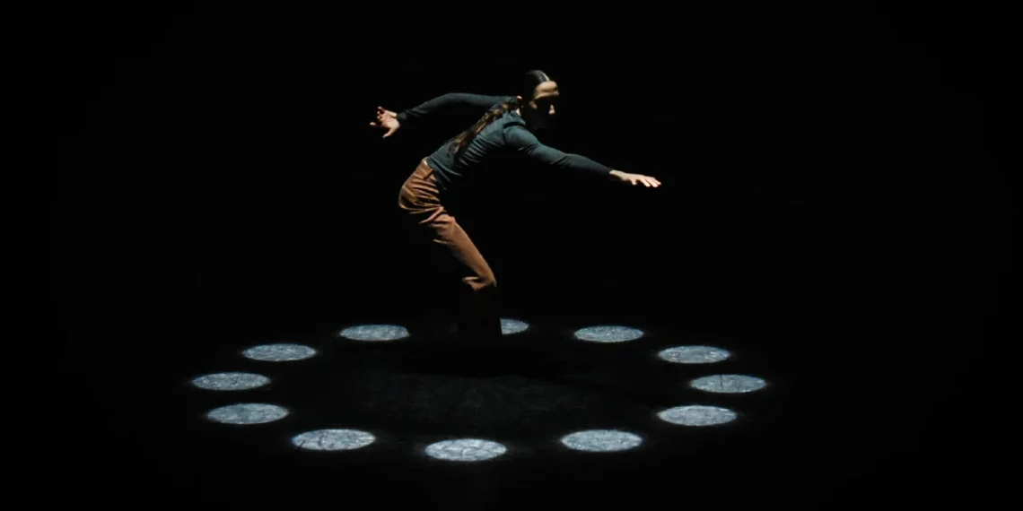 Joshua Beamish/MOVETHECOMPANY Review 2026 featuring Renee Sigouin dressed in dark clothes enclosed in a circle of spotlights on the ground.